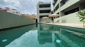 A swimming pool with tiled flooring, surrounded by a building with balconies and a clear sky. - Surf Paraiso @The Point (Los Cerritos, El Pescadero)