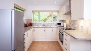 Una cocina moderna con armarios blancos, un refrigerador de acero inoxidable, un microondas y un lavamanos con ventana arriba.