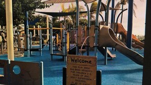 Ein Spielplatz mit verschiedenen Spielgeräten, darunter Rutschen und Klettergerüsten, in einem schattigen Bereich.