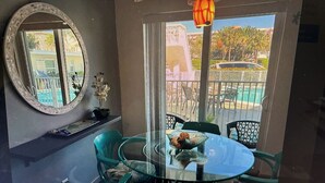 Ein Zimmer mit einem runden Glastisch, Stühlen, einem Spiegel und Blick auf einen Pool und parkende Autos.