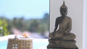 A statue of a seated figure on a pedestal, placed on a glass table near a window with a blurred outdoor view. - INDIGO VILLA Samui - superb sea view! (จ.สุราษฎร์ธานี)