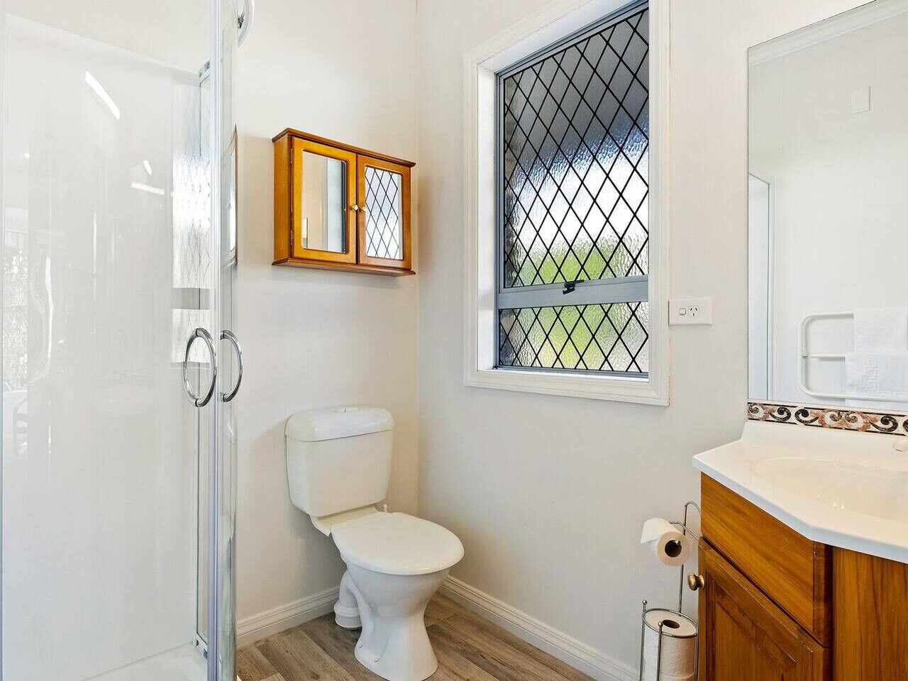 Een badkamer met toilet, douche, wastafel met spiegel, en een raam met metalen tralies.