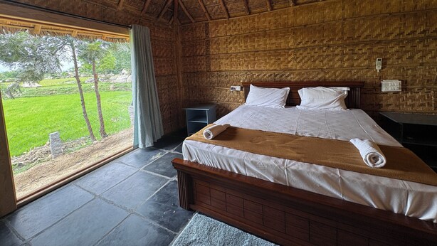 A bedroom with a large bed, a wooden headboard, a nightstand, and a window with a view of greenery.