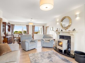A living room with two armchairs, a sofa, a fireplace, and a dining area with a table and chairs.
