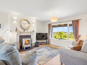 Ein gemütliches Wohnzimmer mit Kamin, einer Couch, einem Teppich und Blick ins Freie.