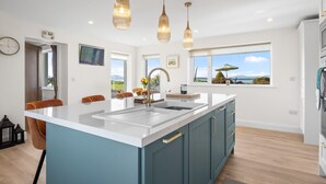 Cozinha moderna com uma ilha grande, luminárias pendentes e vista para o exterior.