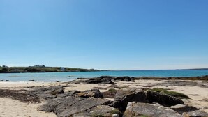 Uma praia rochosa com águas azuis cristalinas e uma linha de costa distante com edifícios.