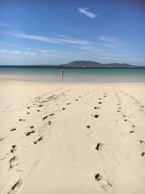 Ein Strand mit Fußspuren, die zum Wasser führen, und eine Person, die in der Ferne steht.