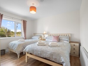 A bedroom with two beds, a window with curtains, a bedside lamp, and a radiator. - Atlantic Haven Water View (Cashel)