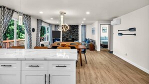 Una cocina moderna con una isla de mármol, iluminación colgante y una zona de comedor con mesa y sillas de madera.