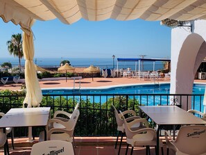 A poolside area with a view of the sea, outdoor seating, and a bar named SanMiguel. - Los Geraneos de Capistrano by Interhome (Nerja)