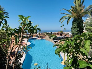 A swimming pool surrounded by lush greenery and palm trees, with a clear view of the ocean in the background. - Los Geraneos de Capistrano by Interhome (Nerja)