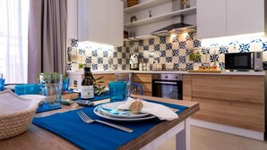 A modern kitchen with white cabinets, a blue and white backsplash, and a dining area with a blue tablecloth. - Vacation Home GIRO DI BITTA (Siculiana Marina)