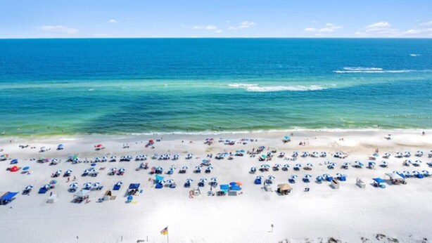 Une plage avec de nombreux parasols et des chaises longues, un ciel bleu dégagé et l’océan.