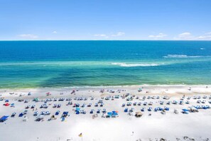 Een strand met veel parasols en ligbedden, een helderblauwe lucht en de oceaan.