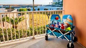 Un balcon avec vue sur la plage, une poussette et un palmier.