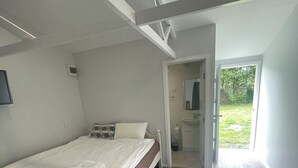 Een slaapkamer met een bed, een klein bureau, een spiegel en een deur naar een balkon.