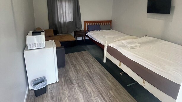 Een kleine kamer met een bed, een bureau, een televisie en een raam met gordijnen.
