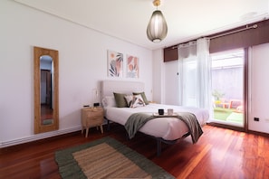 A bedroom with a bed, bedside table, lamp, and a view of the outdoors.