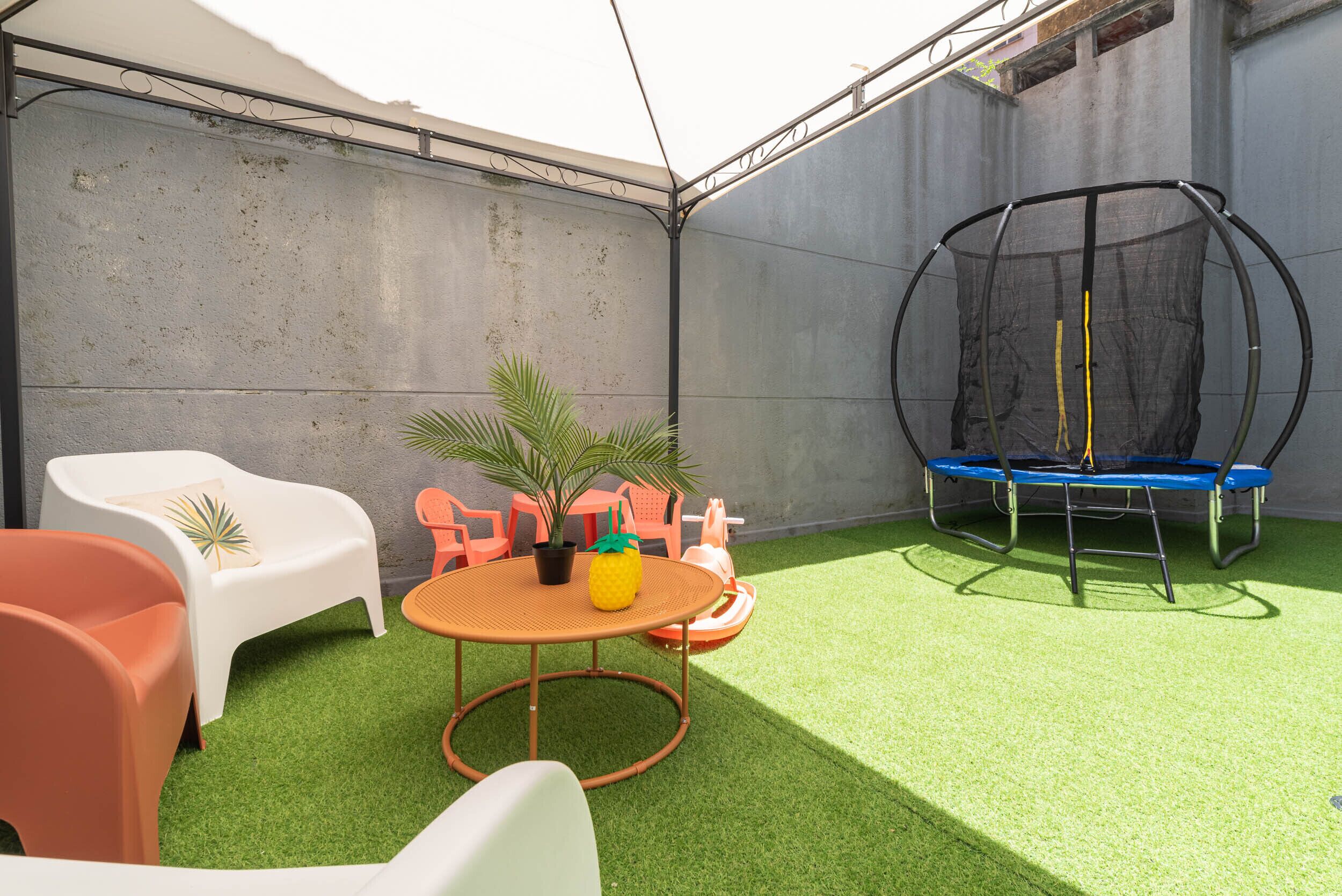 Ein kleiner Außenbereich mit Kunstgrasanlage, einem Trampolin und einem Tisch mit Stühlen.