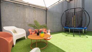 Ein kleiner Außenbereich mit Kunstgrasanlage, einem Trampolin und einem Tisch mit Stühlen.