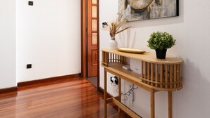 Un couloir doté d’un parquet en bois, une console en bois ornée d’un vase et d’une plante, et un grand tableau abstrait accroché au mur.
