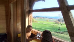 Une cabane en bois dotée d’une grande fenêtre donnant sur un paysage verdoyant.