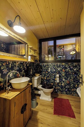 A bathroom with a wooden vanity, a white sink, a toilet, and a red rug. - Uelis-Stoeckli (Meikirch)