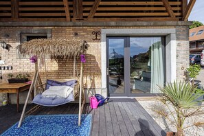 A wooden deck with a hanging chair, a small table with a plant, and a potted plant. - Uelis-Stoeckli (Meikirch)