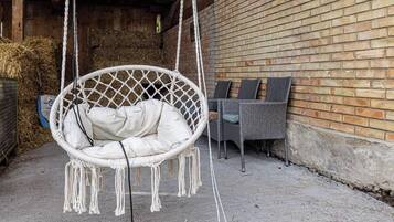 A white hanging chair with a cushion, a wicker chair with cushions, and a brick wall in the background.