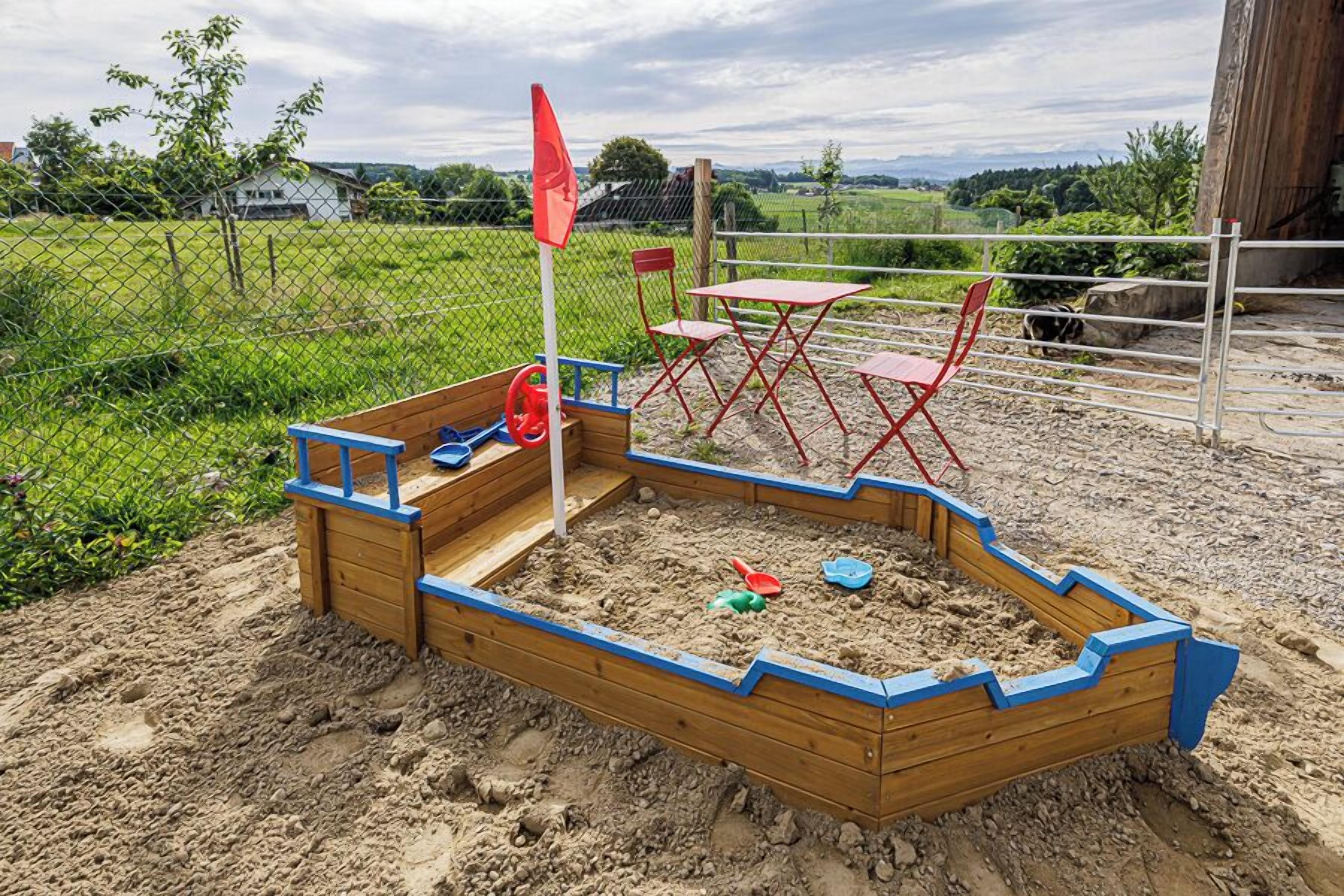 Ein Spielbereich mit Sandkasten, einer Flagge, roten Stühlen und einem Tisch.