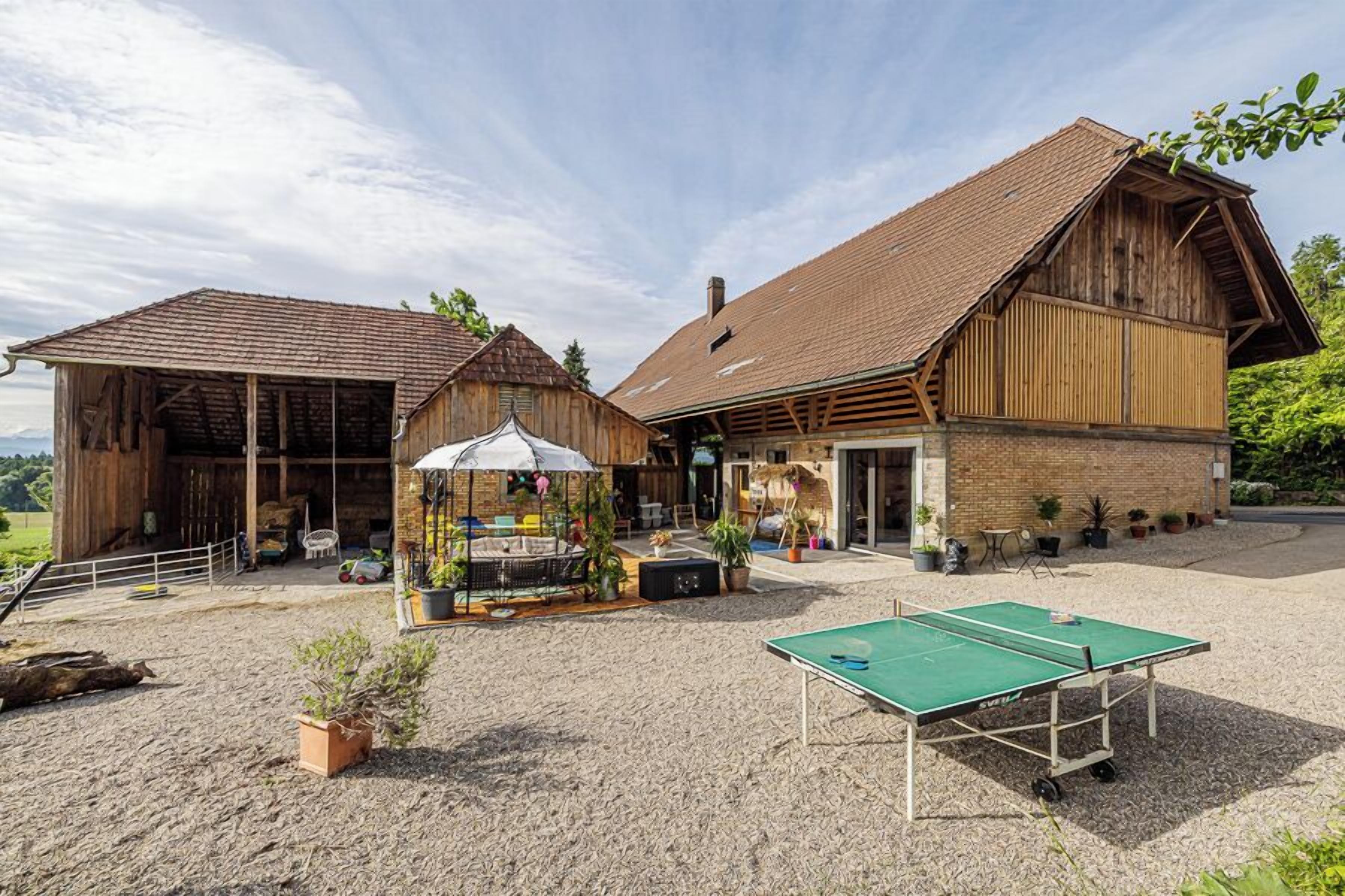 Ein rustikales Bauernhaus mit Tennisplatz davor, umgeben von Kübelpflanzen und Sitzgelegenheiten im Freien.