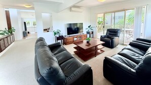 Una sala de estar moderna con un televisor de pantalla plana grande, sofás de cuero, una mesa de centro de madera y una puerta corrediza de vidrio que da a un balcón.