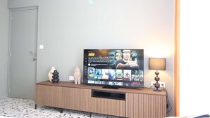 A living room with a flat-screen TV mounted on a wooden cabinet, a lamp on the right, and a door on the left. - ⭐Au calme des Carmes⭐Climatisation⭐Wifi⭐Hypercentre (Avignon)