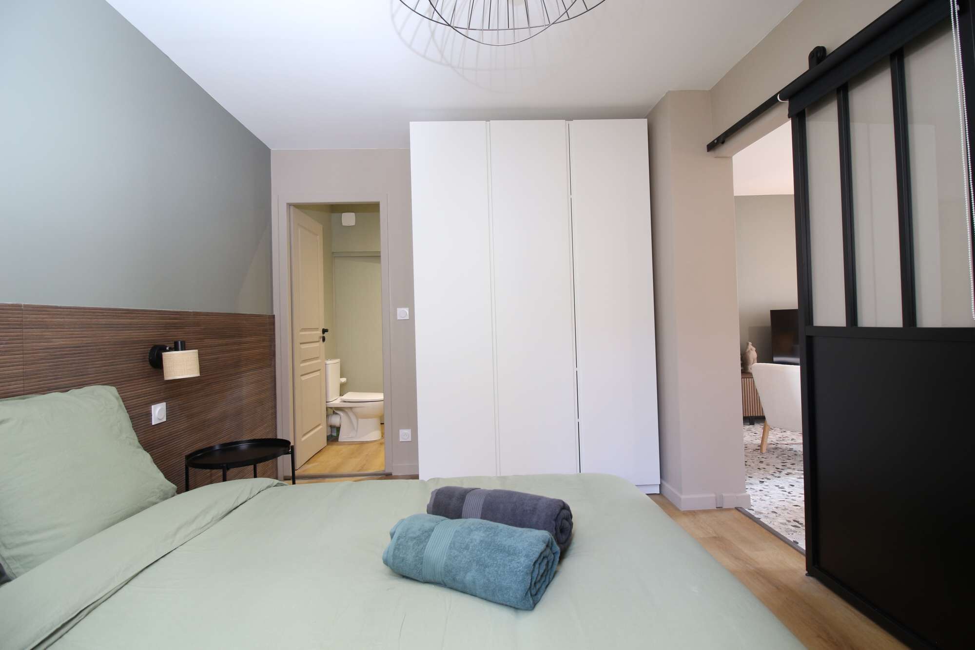 A bedroom with a bed, a nightstand, a wall-mounted lamp, a sliding door to a bathroom, and a TV in the corner.