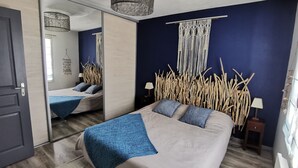 A bedroom with a bed, a mirror, a hanging light fixture, and a wall-mounted macrame piece. - Village house with garden. Pets allowed (La Flotte)