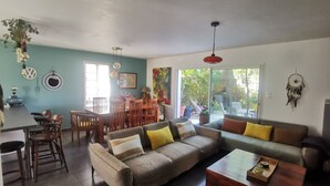 A spacious living area with a sofa, dining table, and chairs, a kitchen area with a dining table and chairs, and a large sliding glass door leading to a garden. - Village house with garden. Pets allowed (La Flotte)