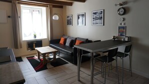 A modern living space with a sofa, dining table, and chairs. There are framed pictures on the wall and a clock.