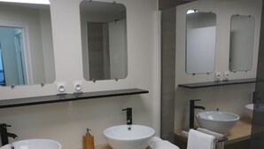 A modern bathroom with two large white sinks, a wooden vanity, a black trash bin, and a glass shower enclosure.