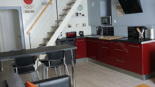 A modern kitchen with red cabinets, a wooden ceiling, and a dining area with a sofa and table.