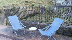 Two metal chairs and a small table on a paved area with a metal fence and a stone wall in the background. - Renovated apartment in quiet country house with view of the Cevennes mountains (Portes)