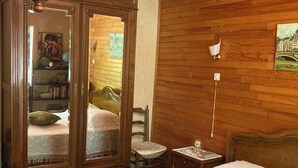 A wooden-paneled room with a bed, a wooden cabinet with glass doors, a small table, and a wall-mounted lamp. - Renovated apartment in quiet country house with view of the Cevennes mountains (Portes)