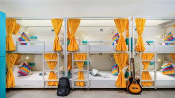 A dormitory room with bunk beds, yellow curtains, a guitar, and a backpack.