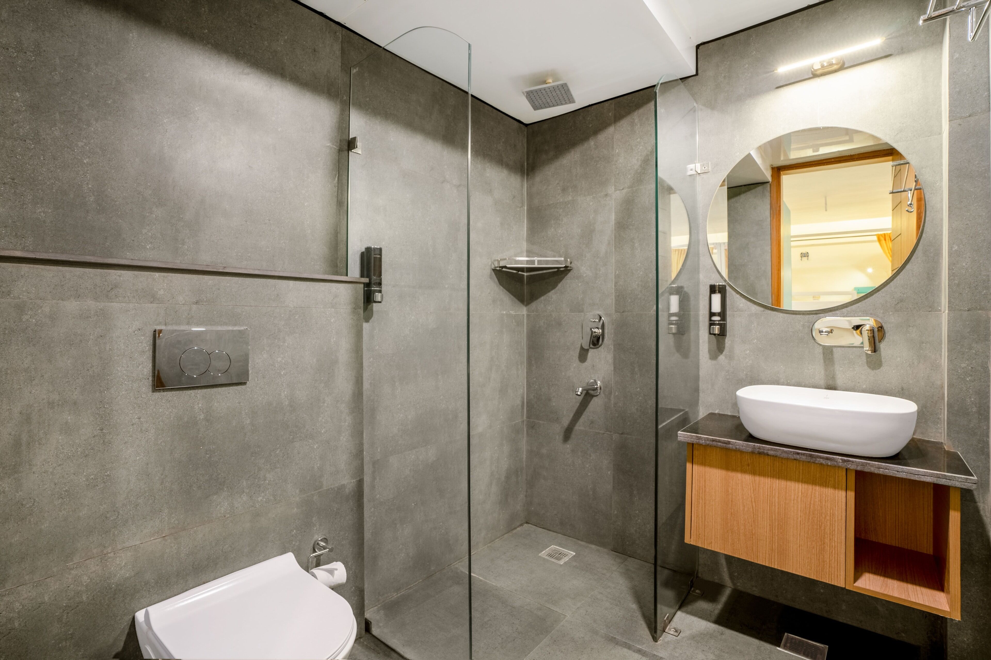 Un baño moderno con ducha de vidrio, lavamanos blanco y tocador de madera.