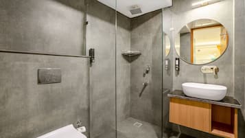 Un baño moderno con ducha de vidrio, lavamanos blanco y tocador de madera.
