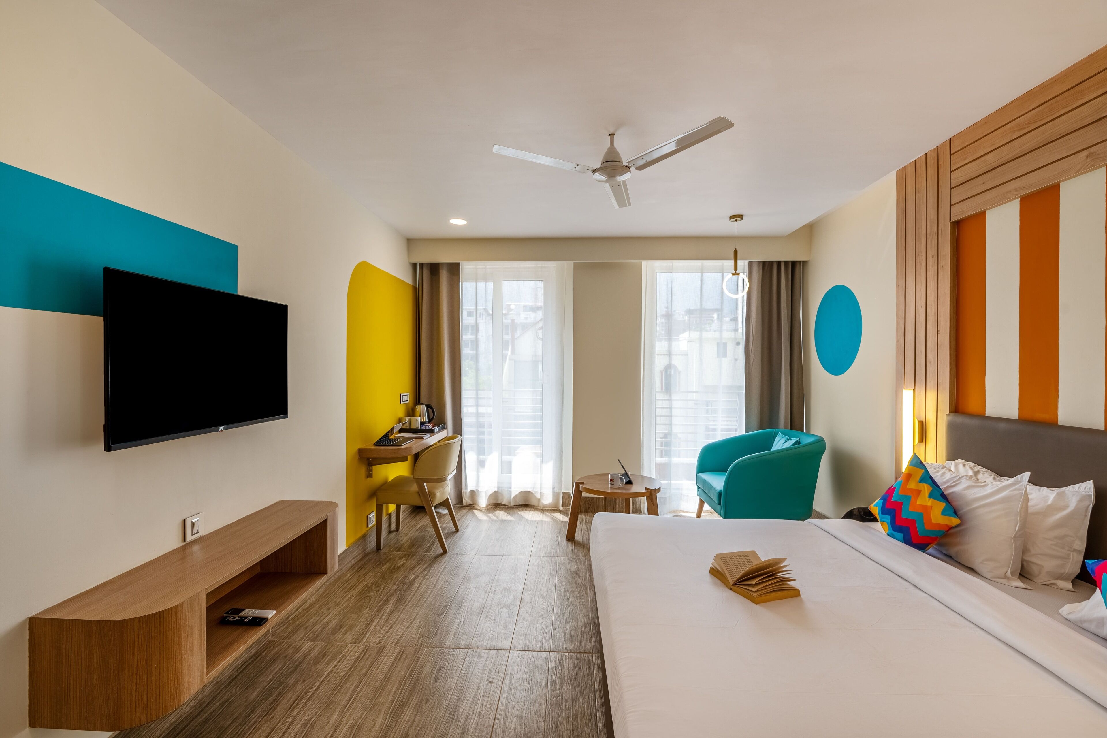 Una habitación de hotel con cama, escritorio, silla, televisor y ventilador de techo.