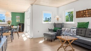 A modern living room with a grey sofa, a wooden coffee table, and a dining area with a table and chairs.