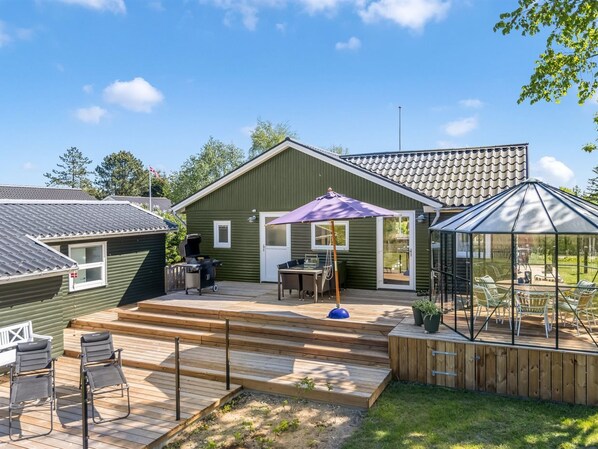 A green house with a patio, a grill, and a covered seating area.