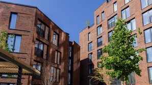 Un edificio moderno con un patio, que presenta una combinación de fachadas de ladrillo y cristal, mobiliario exterior y vegetación.