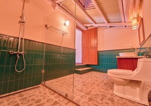 Un baño con azulejos verde y beige, un inodoro blanco y una ducha.